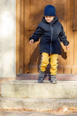 The little boy opens the big brown entrance door. The child leaves the house for an autumn walk.の写真素材