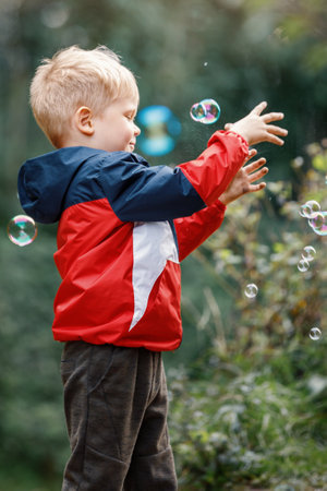Cute little boy playing with soap bubbles in park. The child catches and bursts soap bubbles with his hands.の写真素材