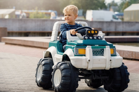 Cute little boy driving big electric toy car with steering wheel and having fun outdoors.の写真素材