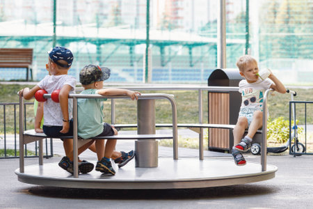 Group of happy kids having fun on roundabout at playground. Carousel for children in summer in the park.の写真素材