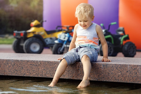 Little boy plays and cools feet in fountain water on a hot summer day.の写真素材