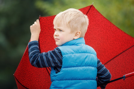 Close up portrait of boy in blue raincoat hold umbrella in the rainy day.の写真素材