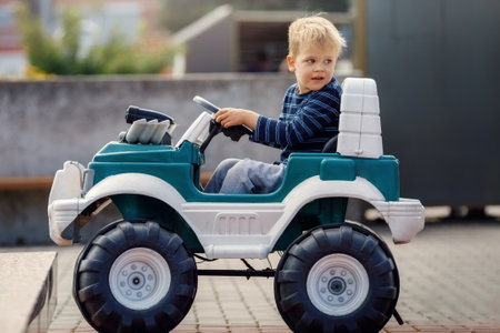 Funny boy car driver with the steering wheel. Three year-old boy in a blue sweater in a green toy car in the city. Little boy driving big toy car and having fun, outdoors.の写真素材
