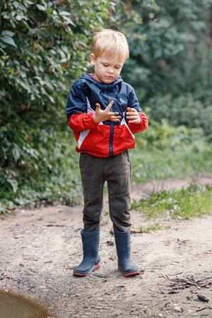 A little boy explores the mud near a puddle during a walk in nature, he looks at his smeared hands.の写真素材