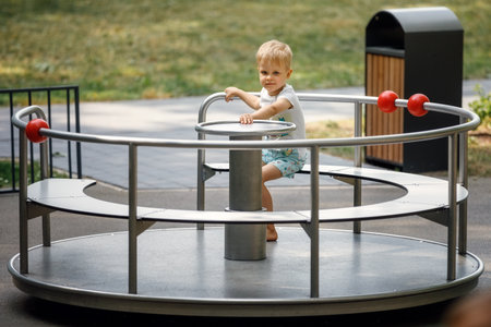 A little boy sits in a metal carousel for children in summer in the park and poses for the camera.の写真素材
