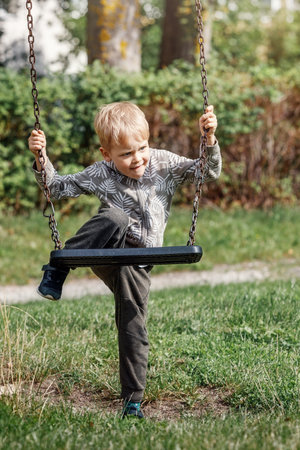 The blond boy plays with a chain swing as he tries to climb on it without his parents help.の写真素材