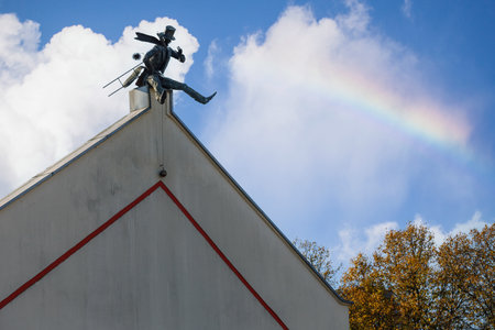 Chimney Sweeper Sculpture on roof in old town of Klaipeda, Lithuania. House wall in Klaipeda Old Town. Blue sky with white clouds and rainbow.のeditorial素材