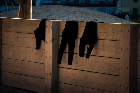 Three black wetsuits drying on a wooden fence at the end of the day.の写真素材
