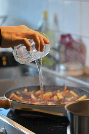Photo of food being cooked in kitchen, frying vegetables in pan and adding waterの写真素材