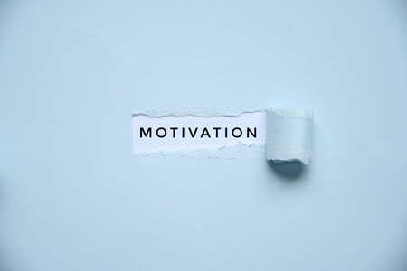 Overhead of a light blue paper with a hole where text says motivationの写真素材
