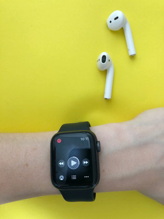 Overhead of a smart watch and wireless earphones on yellow background