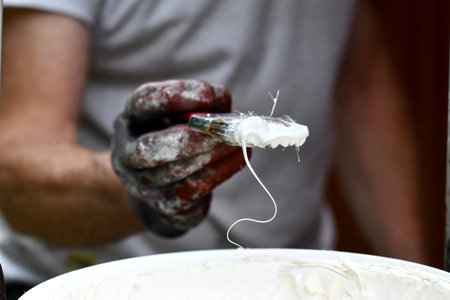 Photo of a man applying white color on a paintbrush to paint house exterior