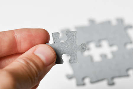 Photo of a person adding last piece of jigsaw puzzle to fit together on white backgroundの写真素材
