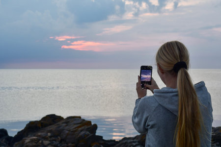 Landscape photo of a woman or person photographing ocean or sea at sunset or sunriseの写真素材