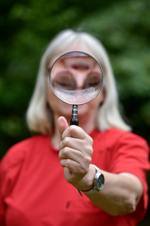 Portrait of a woman holding a magnifying glass in front of her face while wearing a red t-shirtの写真素材