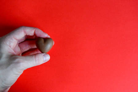 Photo of red jelly candy heart in hand of woman on red backgroundの写真素材