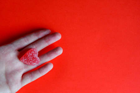 Photo of red jelly candy heart in hand of woman on red backgroundの写真素材