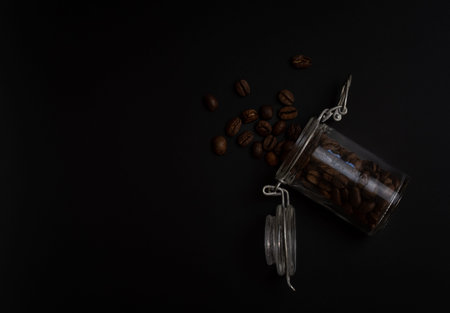 Studio photo of brown coffee beans in a glass jar on black backgroundの写真素材