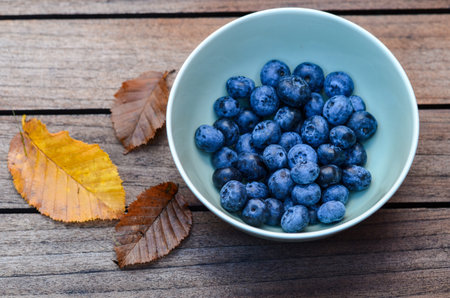 Photo of blueberries in a bowl and leaves on a tableの写真素材