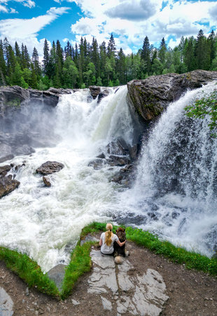 Aerial view of woman and dog watching large waterfall in summerの写真素材
