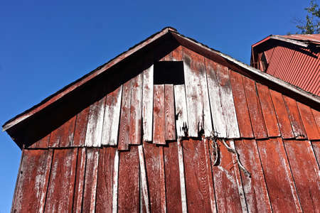 Pocono Mountains, Pennsylvania: The peak of an abandoned barn with peeling red paint against a deep blue sky.の写真素材