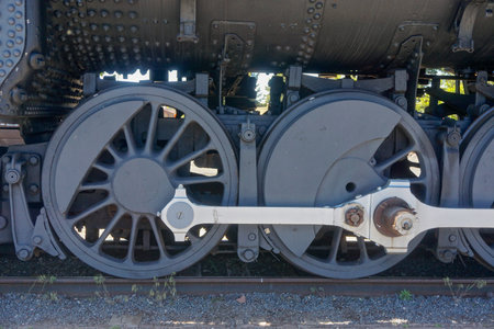 Close-up of the wheels of a locomotive; charcoal grey with bright metal pistons.