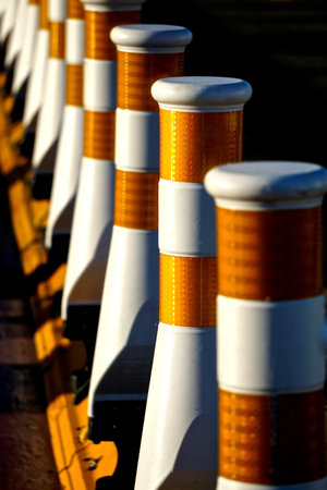 Close-up of a row of white traffic safety lane dividers with orange reflectors, in bright sunlight.