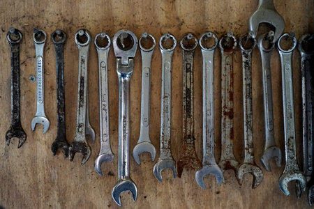 Closeup of a collection of well-used wrenches hanging from nails on the wooden wall of a barn.