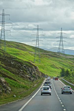 Power lines and towers under a cloudy sky, along a highway in the Highlands of Scotland.の写真素材