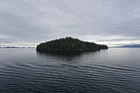 Sitka, Alaska, USA: Dawn on the horizon and thick clouds in the sky above a small isolated island in...