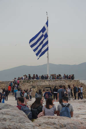 Athens, Greece: Tourists gather around the Greek flag at the Acropolis of Athens, under a hazy sky caused by dust pollution.のeditorial素材