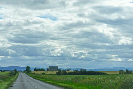 A thick cover of clouds over a highway in the Highlands of Scotland, with an old church on the side of the road.のeditorial素材