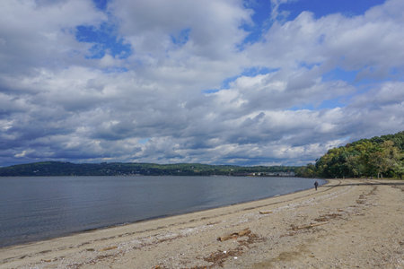 Croton-On-Hudson, New York, USA: A solitary person walks along the Hudson River under a cloud-filled...