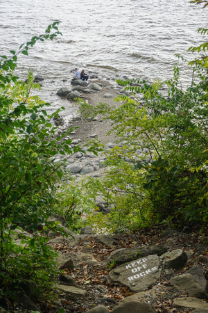 Croton-On-Hudson, New York, USA: A young couple sits on rocks at the shore of the Hudson River...