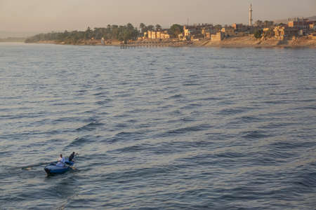 Nile River, Egypt: Two men in a rowboat, a minaret, and houses along the east bank of the Nile River at sunset.のeditorial素材