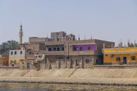 Nile River, Egypt: Colorful houses, date palm trees, carpets drying in the sun, and a minaret along the east bank of the Nile River.のeditorial素材