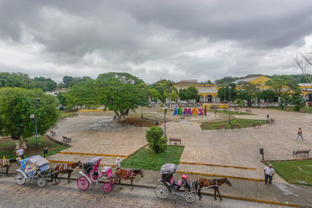 Izamal, Yucatan, Mexico: Horses and carriages wait for passengers along the main plaza of Izamal, under a cloudy sky.のeditorial素材