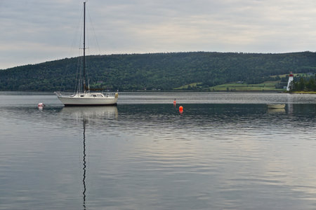 Baddeck, Nova Scotia, Canada: Sailboat anchored in Bras dOr Lake on Cape Breton Island, with the Kidston Island Lighthouse, 1912, on the right.の写真素材