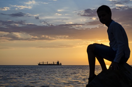 The ship that is laying a gas pipe on the sea bottom against the sunset and silhouette of the teenagerの写真素材