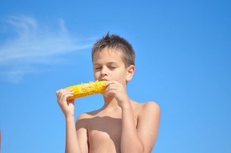 Teenager eats corn on the sky backgroundの写真素材