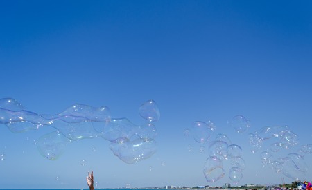 Soap bubbles against blue sky and sea with handの写真素材