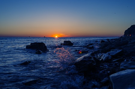 Bright sunset under the sea with waves splashes and stones.の写真素材