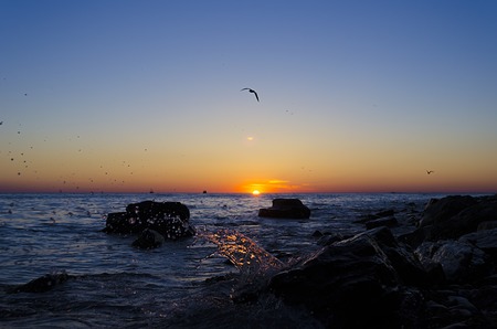 Bright sunset under the sea with waves splashes and stones.の写真素材