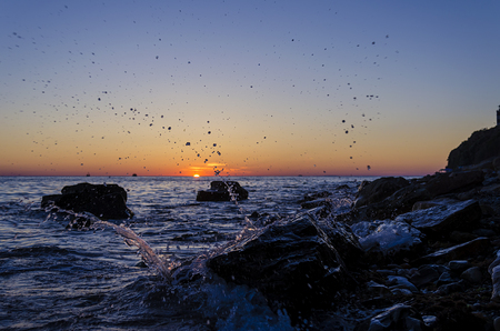 Bright sunset under the sea with waves splashes and stones.の写真素材