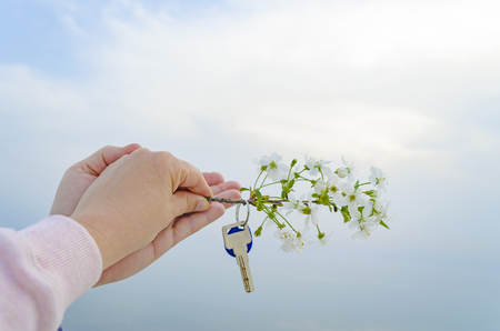 The key is from a new house and a cherry blossom branch in hands on a sunset background.の写真素材