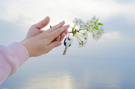 The key is from a new house and a cherry blossom branch in hands on a sunset background.の写真素材