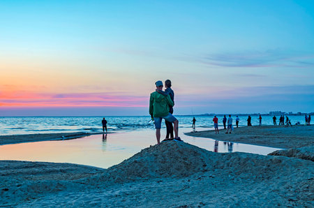 Tourists and fishermen are on the black sea and admire the beautiful sunset. A couple in love takes a selfie against the sunset.の写真素材