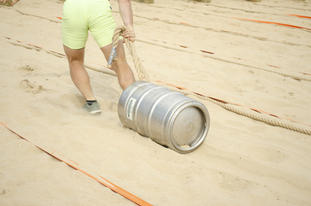 A man in shorts pulls a rope tied with rope over the sand. Sport competitions.の写真素材