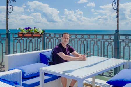 Healthy sports man aged is sitting in an outdoor cafe with blue sea background on vacation or...