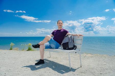 A healthy athletic elderly man sits on a bench and looking at the sea.